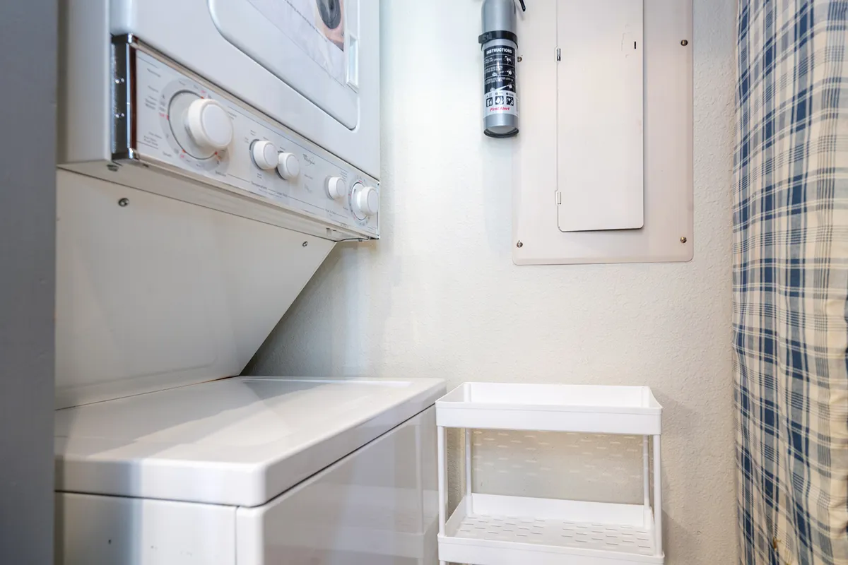 This image features a laundry area with a washing machine, dryer, storage container, and wall panel. The space is practical and efficiently organized, highlighting a key family-friendly amenity.