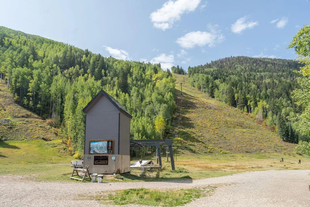 This image features the exterior of a small building adjacent to a ski lift, surrounded by trees. The scene highlights immediate access to skiing, suggesting the convenience of a true ski-in, ski-out property. The tranquil natural setting reinforces the adventure base theme.