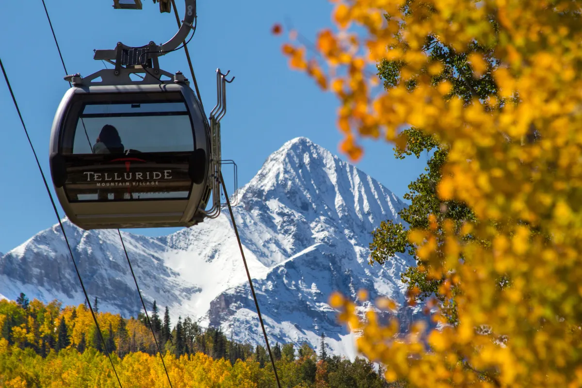 A gondola soars above vivid autumn foliage and a snow-capped mountain, encapsulating Telluride’s exhilarating outdoor adventures and spectacular seasonal scenery.