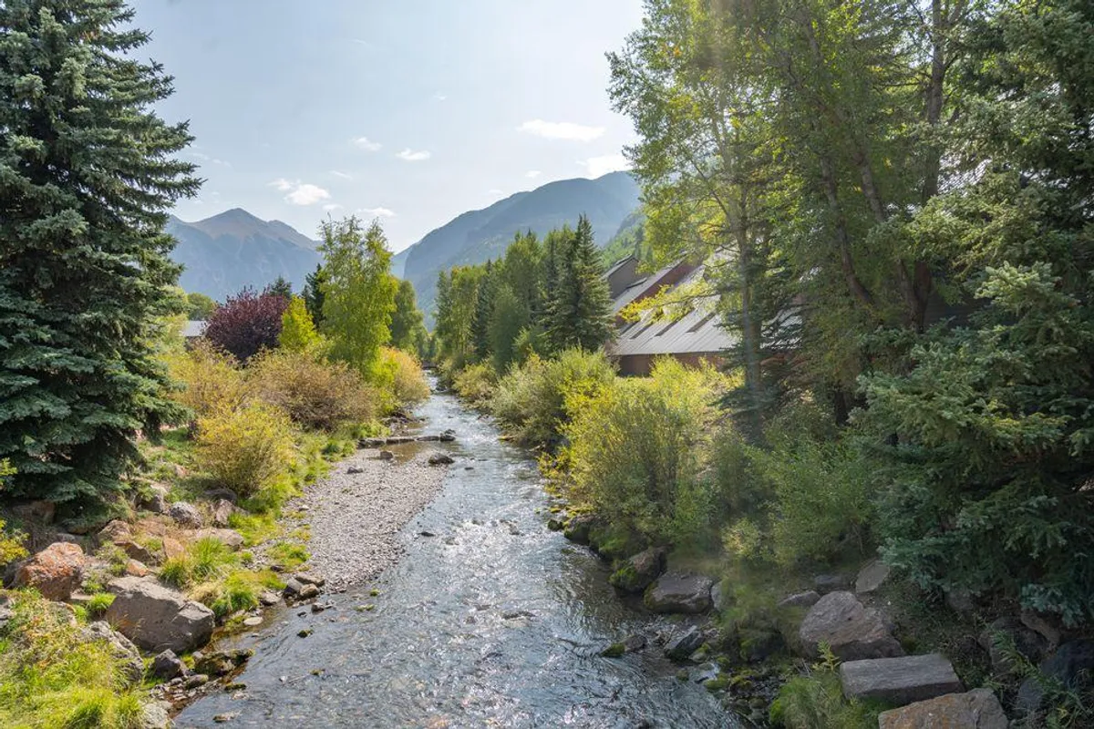 A scenic view of a flowing river bordered by lush trees, with a picturesque mountain backdrop and a well-maintained pathway along the water's edge. The path appears gentle and accessible, inviting families for easy strolls or nature walks.